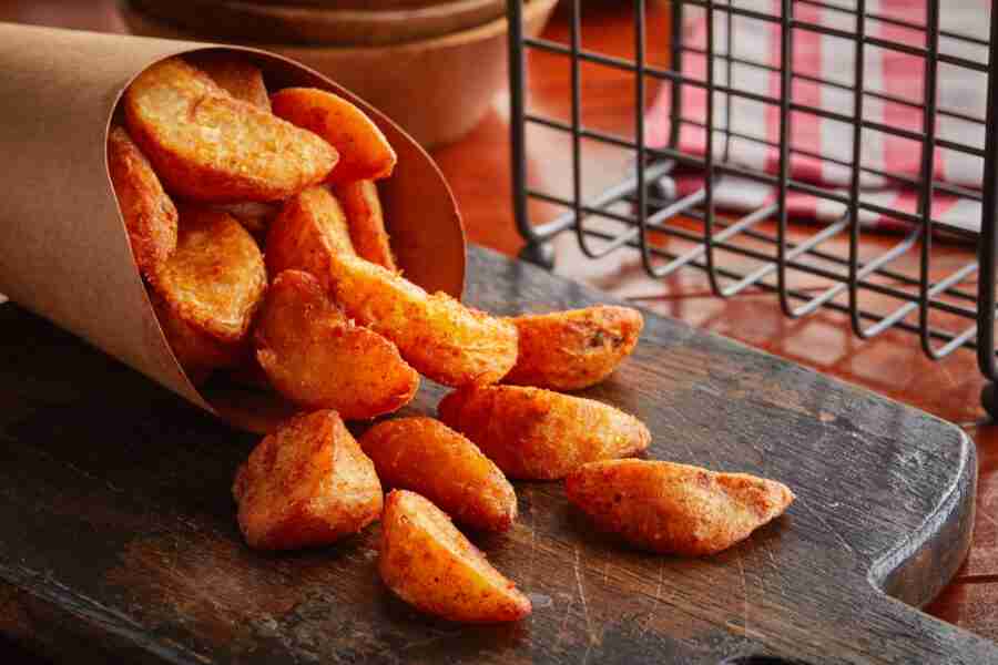 Potato Wedges served in a dish isolated on wooden background side view