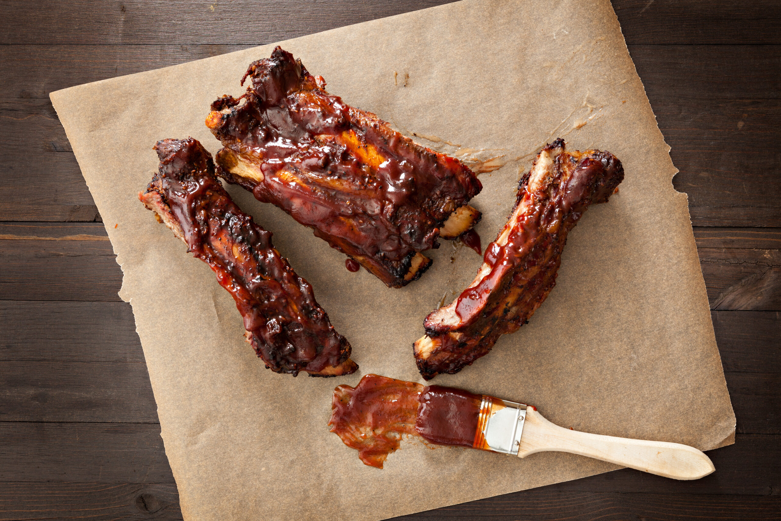 A close up shot of several barbecued ribs and a sauce brush.