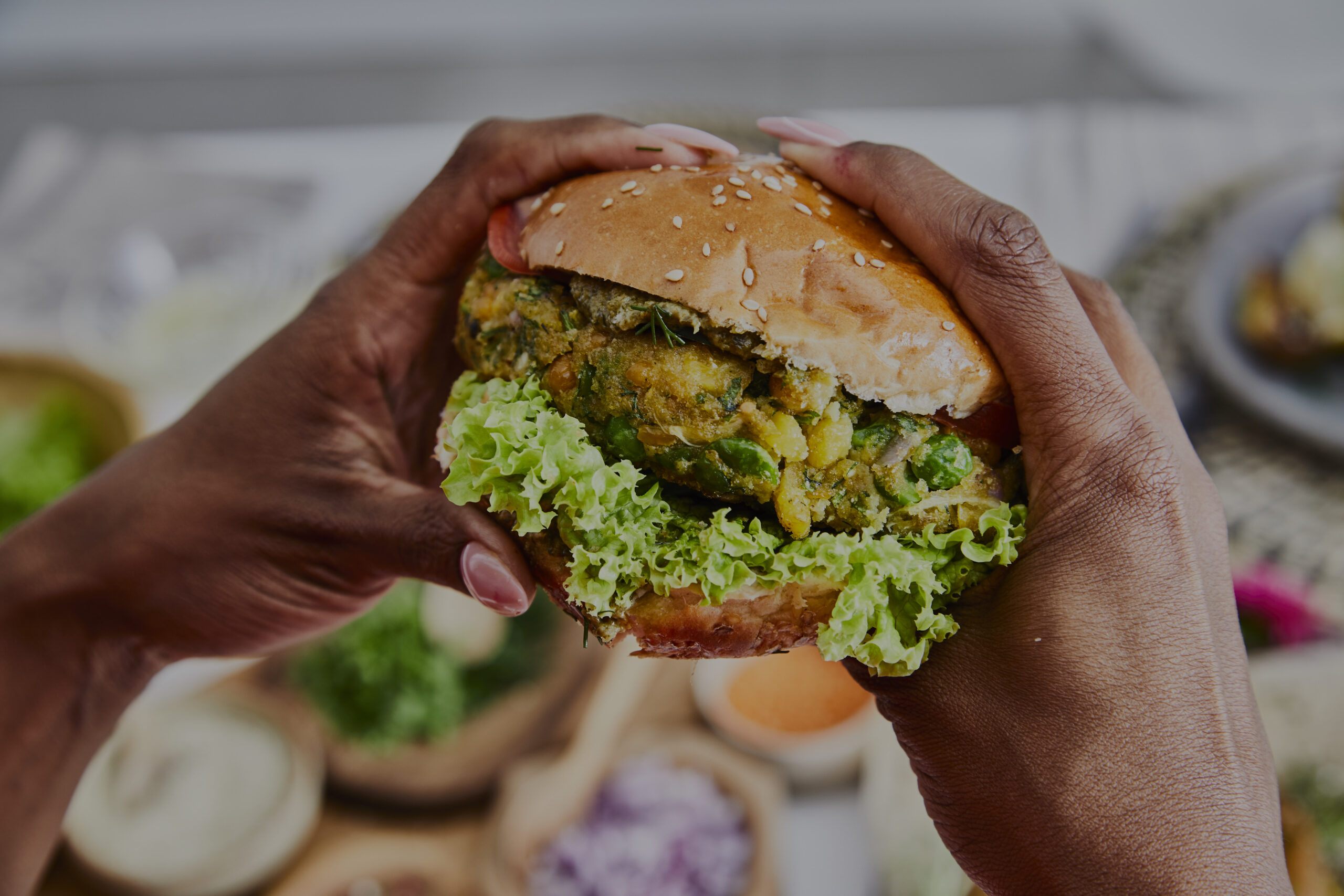 A woman holding a healthy vegan burger, made of green peas, chickpea, corn, fresh seasoning, herbs and spices