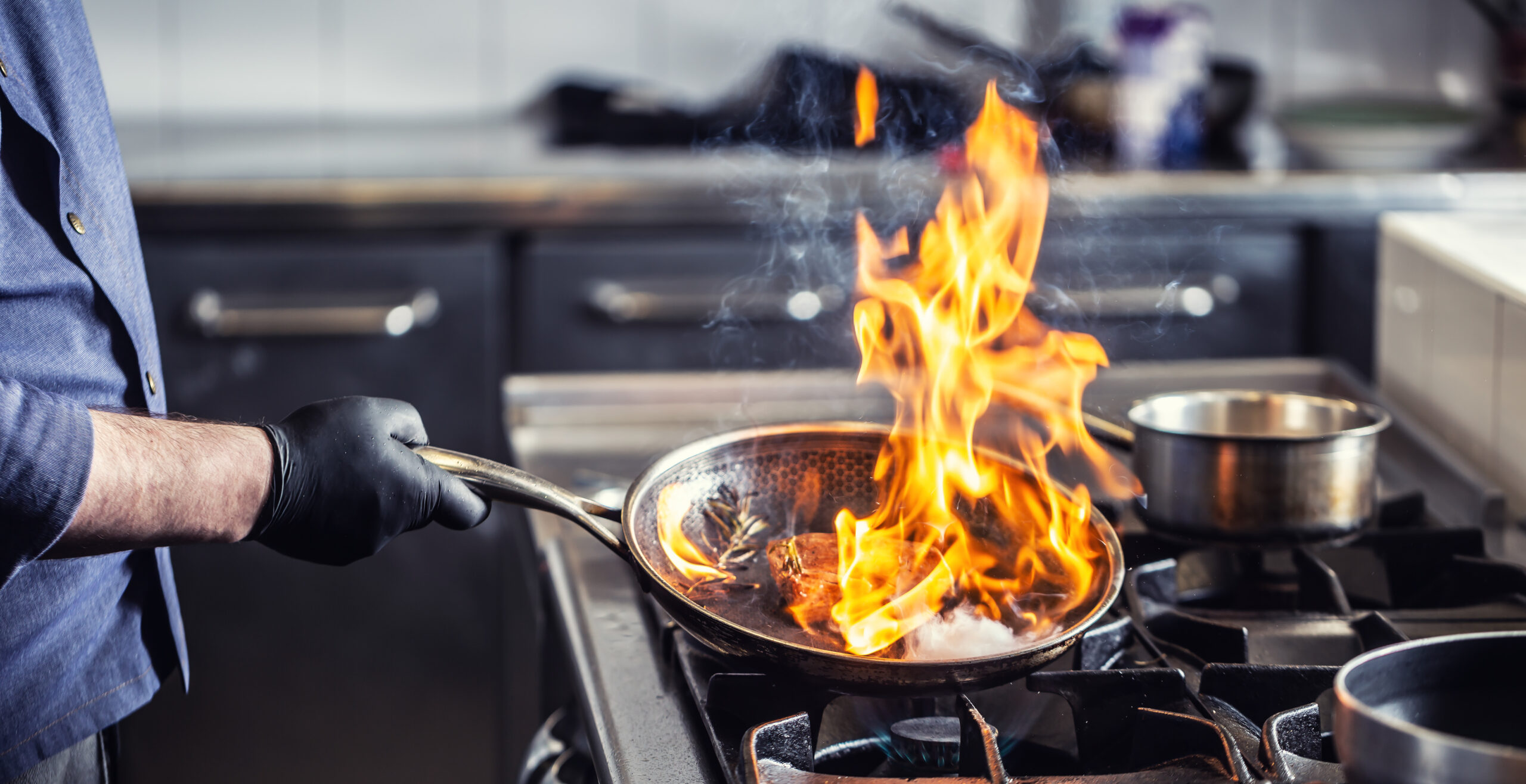 Chef holding pan performing flambe on a dish in it.