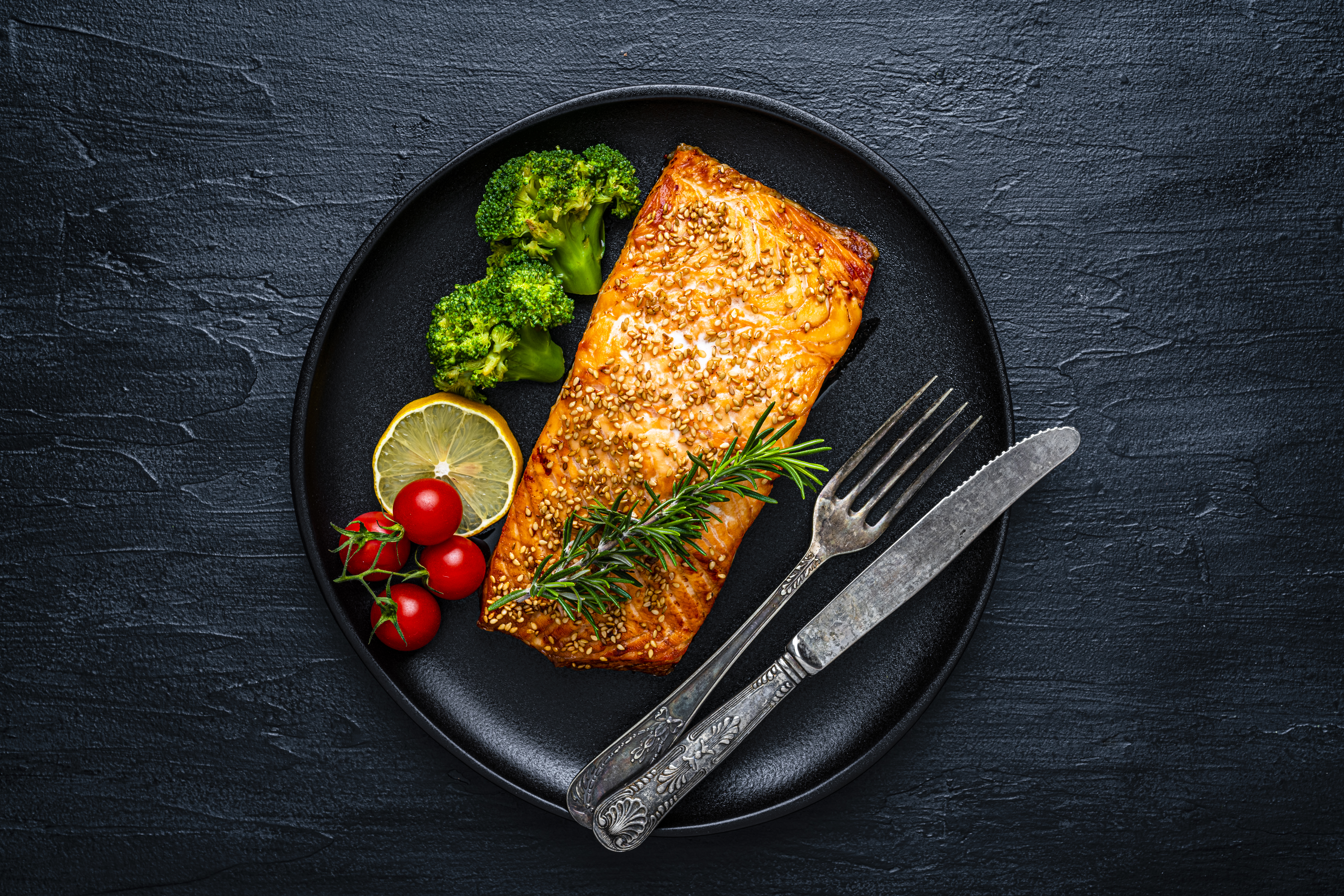 Healthy eating: overhead view of a baked salmon fillet with sesame seeds and vegetables. High resolution 42Mp studio digital capture taken with SONY A7rII and Zeiss Batis 40mm F2.0 CF lens