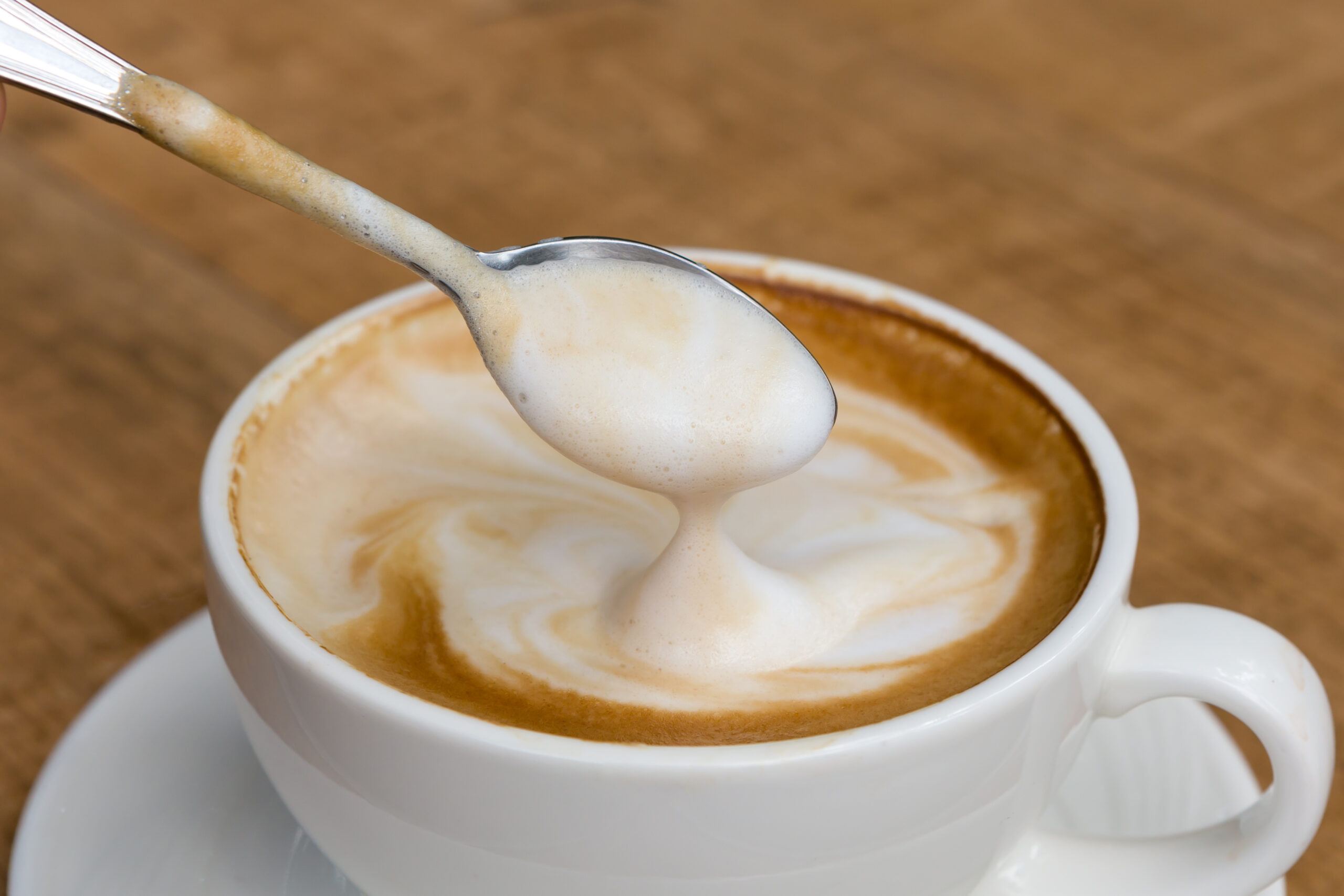 Latte coffee in white coffee cup with plate and spoon on white background, Closeup