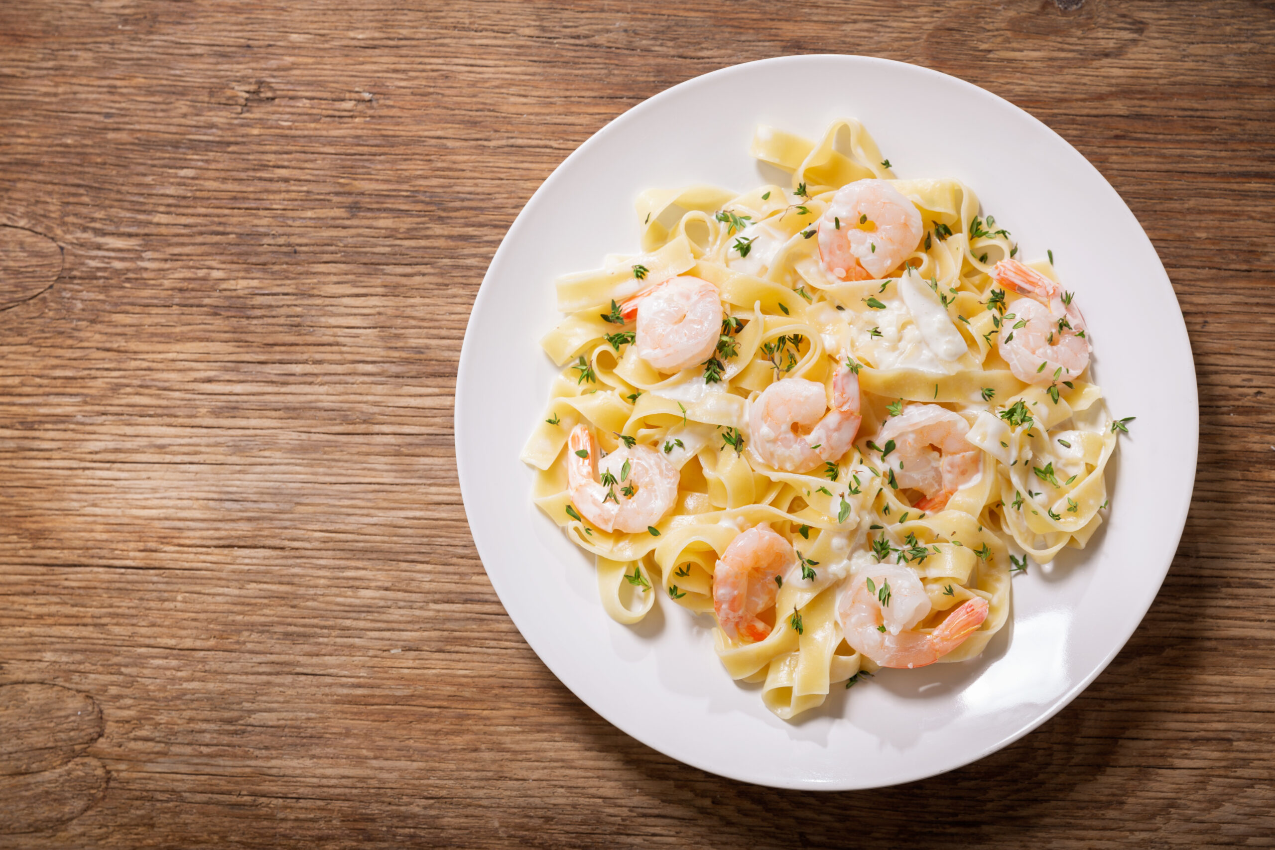 plate of pasta fettuccine with cream sauce and shrimps on a wooden background, top view