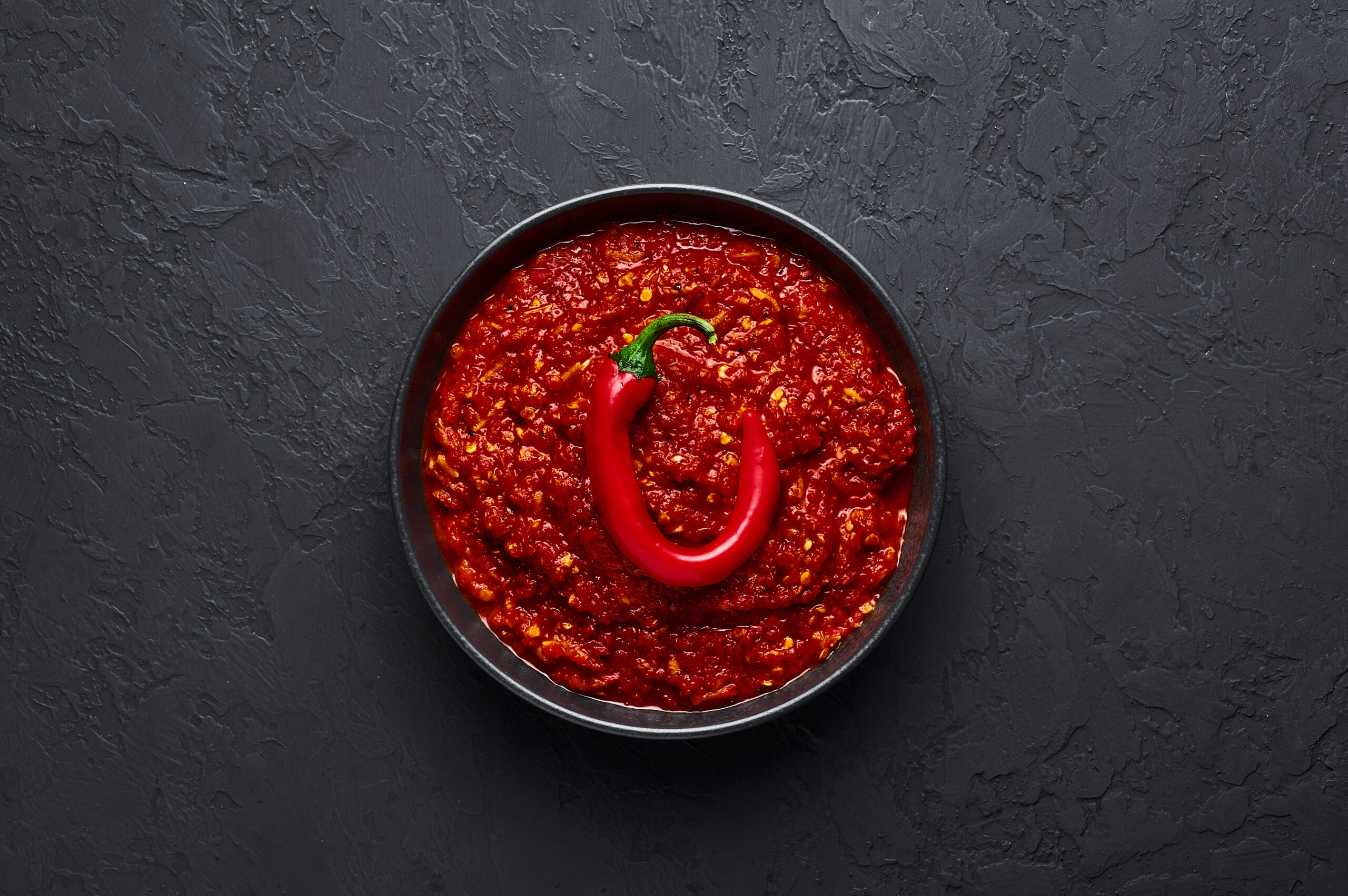 Schezwan Sauce in black bowl at dark background. Schezwan Sauce is Indo-chinese or Sichuan cuisine hot sauce with red chilli, garlic and ginger.