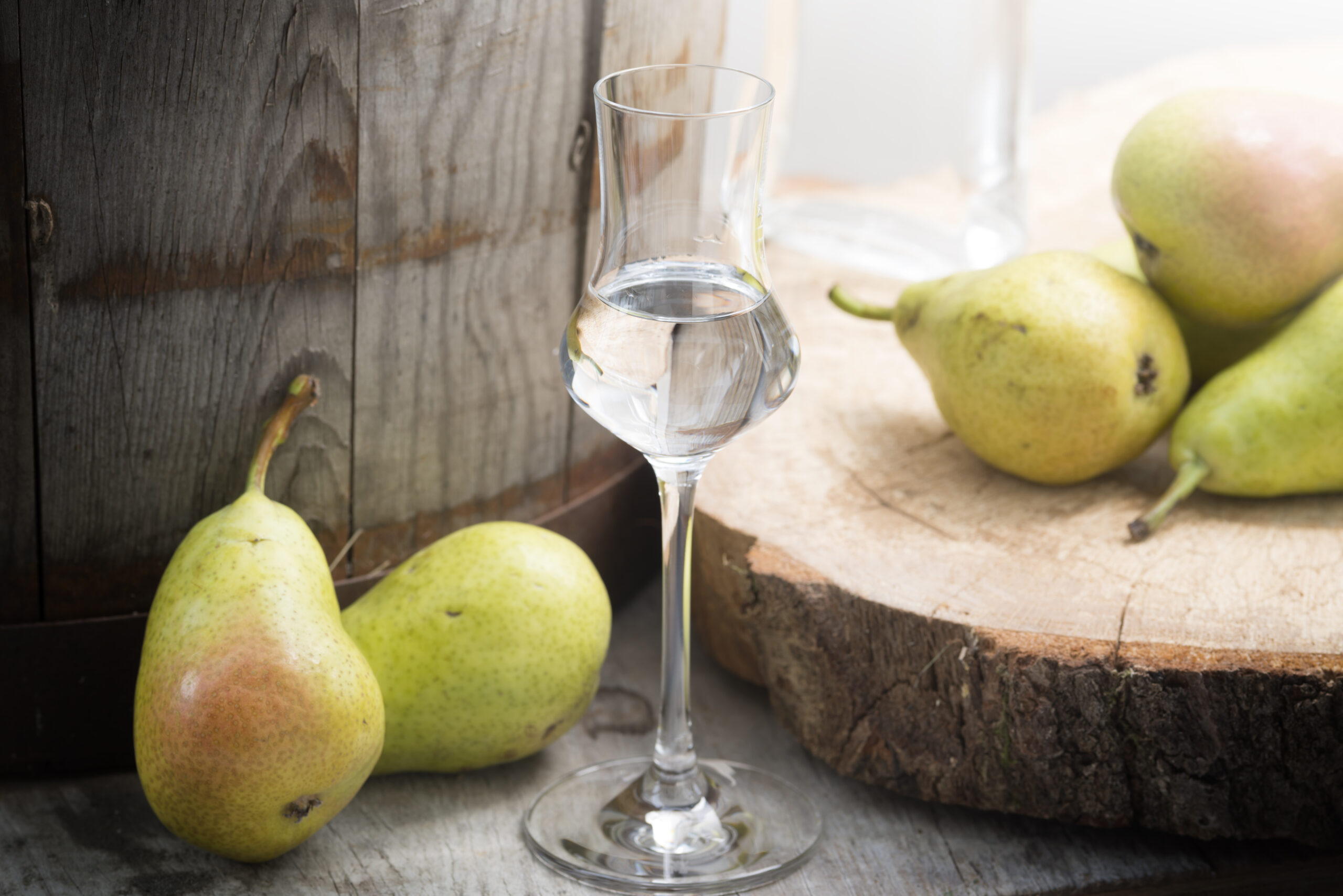 A bottle of pear fruit brandy on a wooden table in a garden. Selective focus on the glass