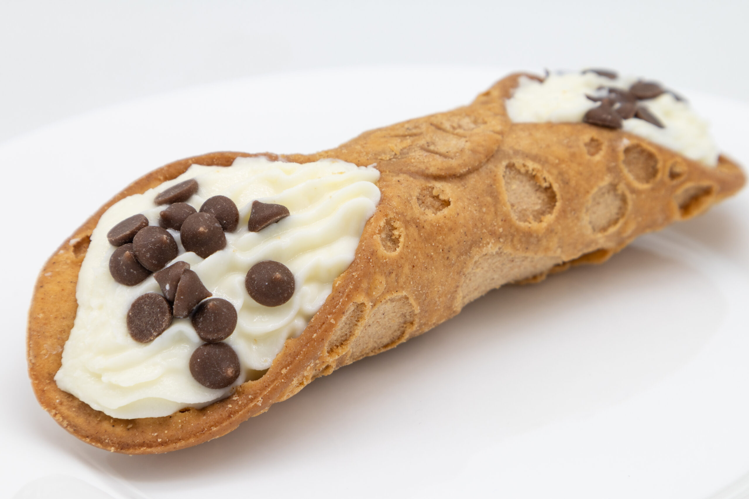 A closeup of a traditional Sicilian cannoli on a white plate with a white background
