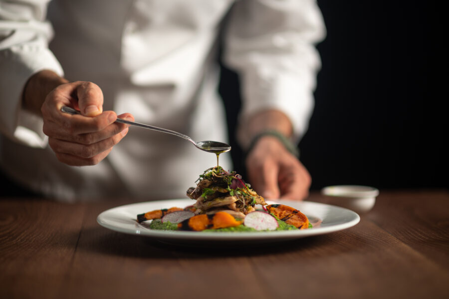 A male chef pouring sauce from the spoon on meal on a black background.