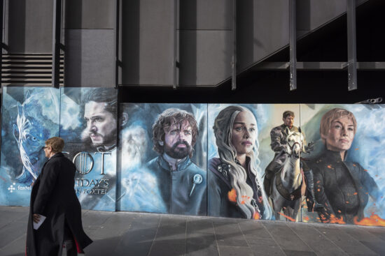 A pedestrian in the city center of Melbourne, Australia, walks past a colorful advertisement for the Game of Thrones series airing on Foxtel, an Australian pay television company. The ad shows the characters played by the actors Kit Harington, Peter Dinklage, Emilia Clarke, Nikolaj Coster-Waldau, and Lena Headey. (August 2017)