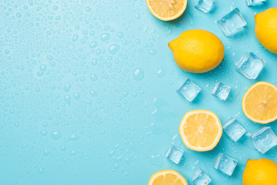 Above photo of yellow lemons cubes of ice and drops isolated on the blue background with empty space