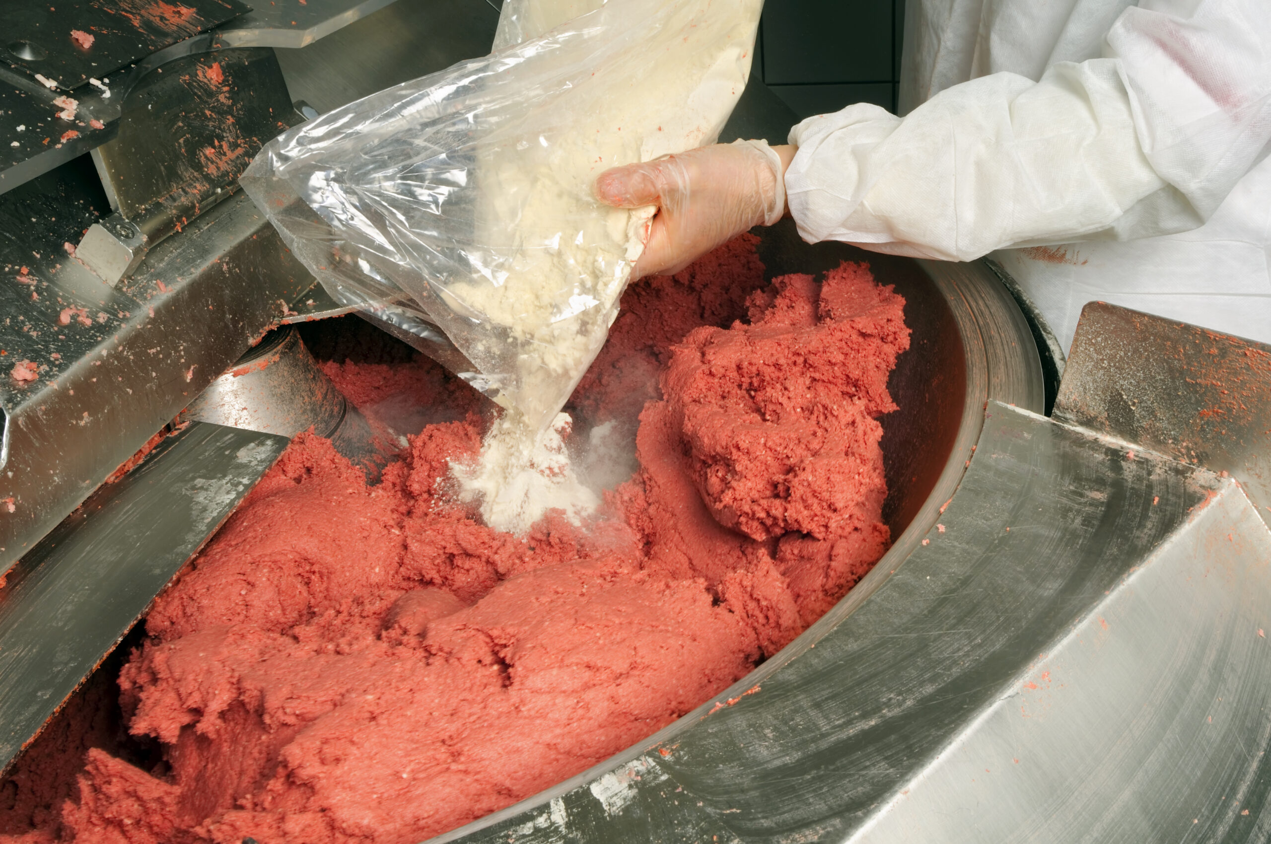 Butcher is mixing meat and spices to make salami in food processing plant..