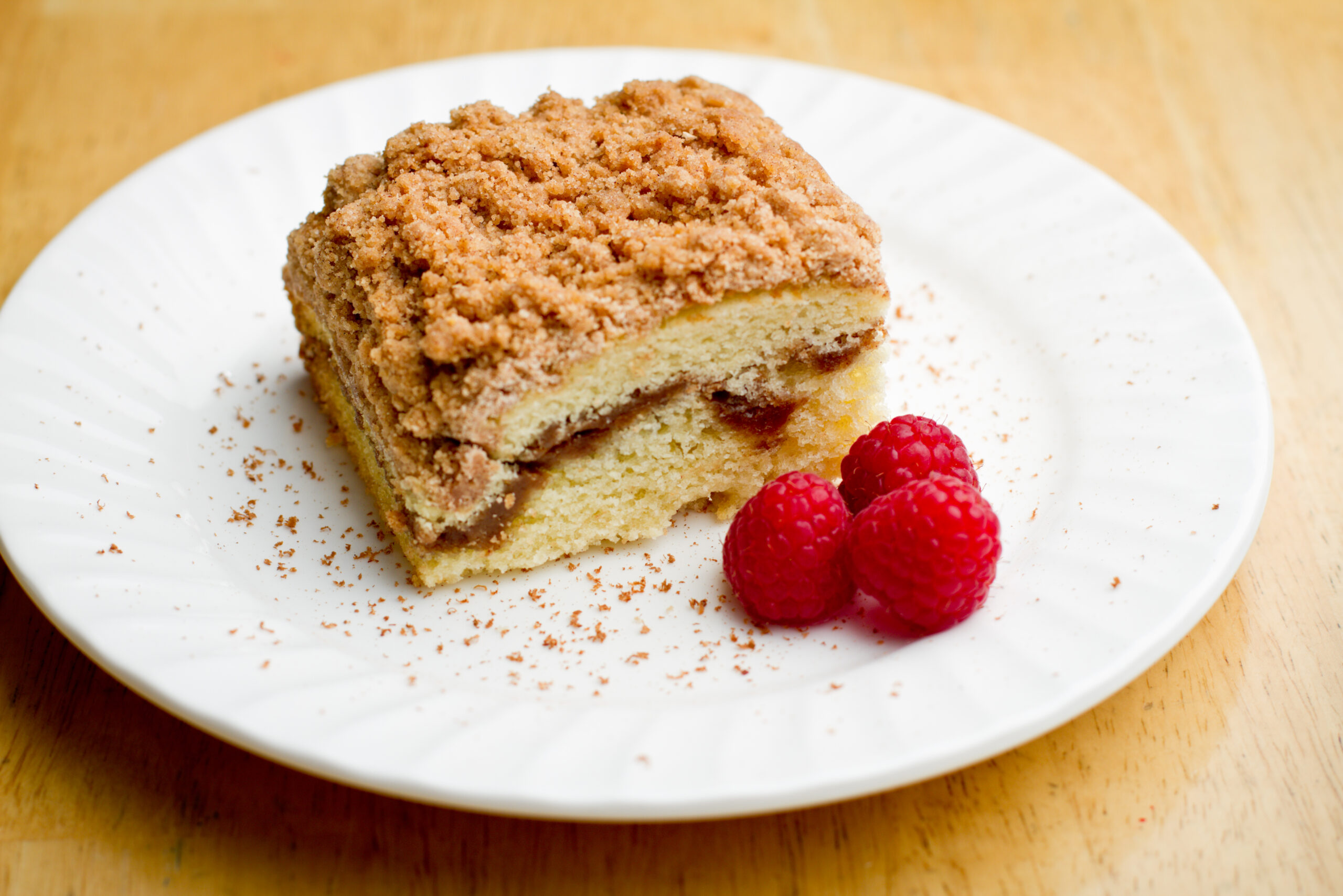 Coffee Cake with Cinnamon and Raspberries arranged on a white plate with ground cinnamon on the plate