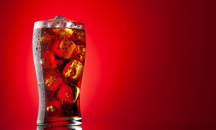 Cola with ice. Fresh cold sweet drink with ice cubes. Over red background with copy space