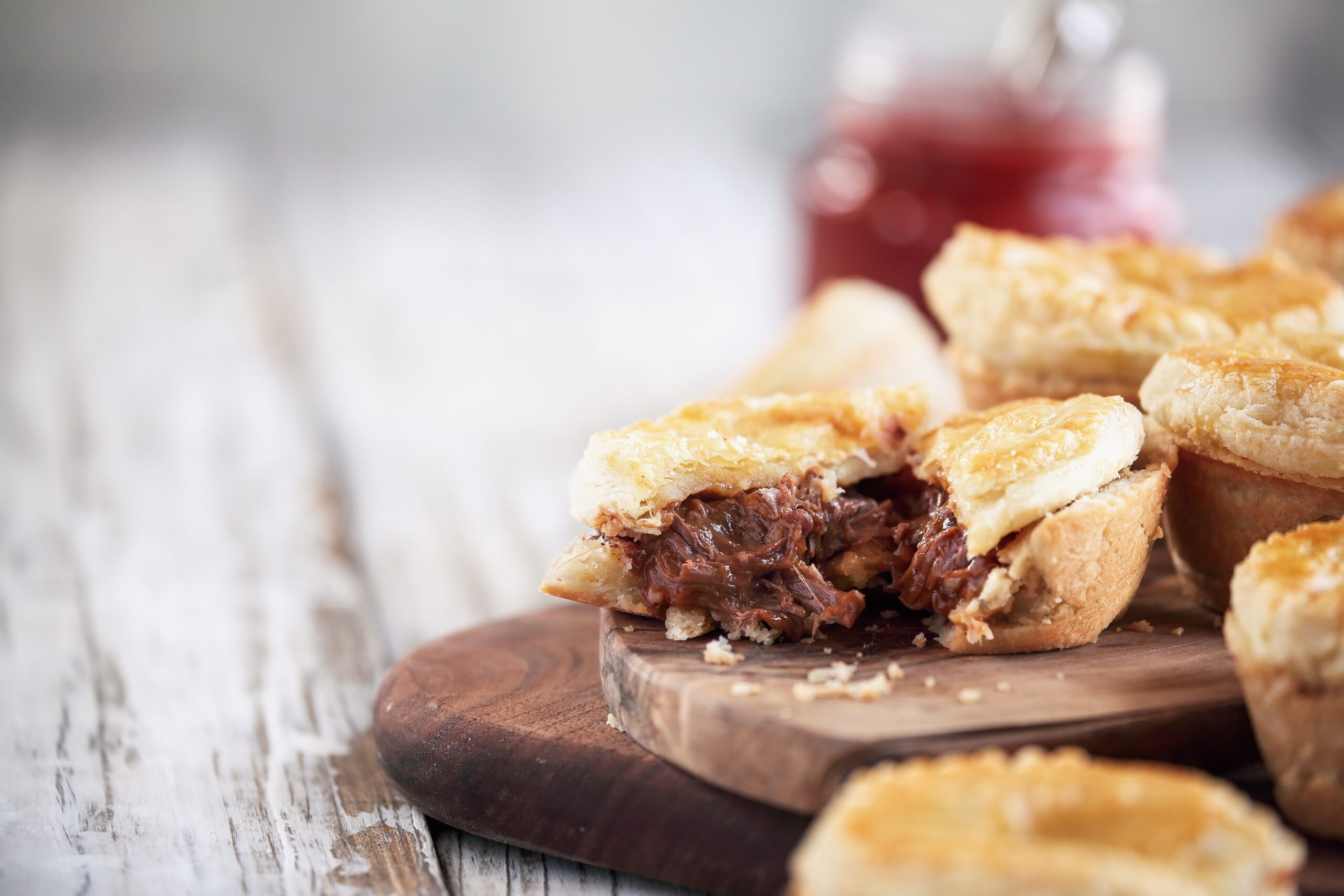 Cut fresh venison meat pies on a rustic wood cutting board with filling visible and ketchup in the background. Selective focus on center pie with extreme blurred foreground and background. Free space for text available.