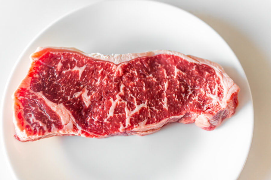 Flat top view of raw red strip or ribeye steak cut closeup of texture butcher cut on white plate and background