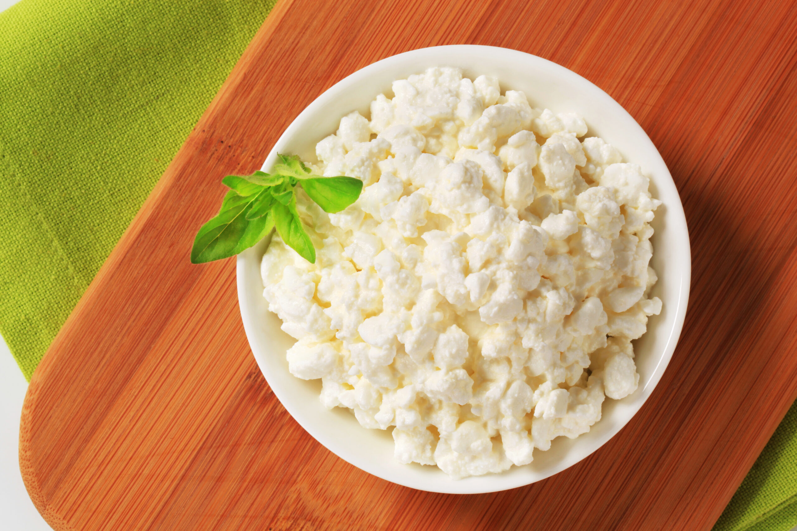 fresh cottage cheese in a small white bowl on a wooden cutting board