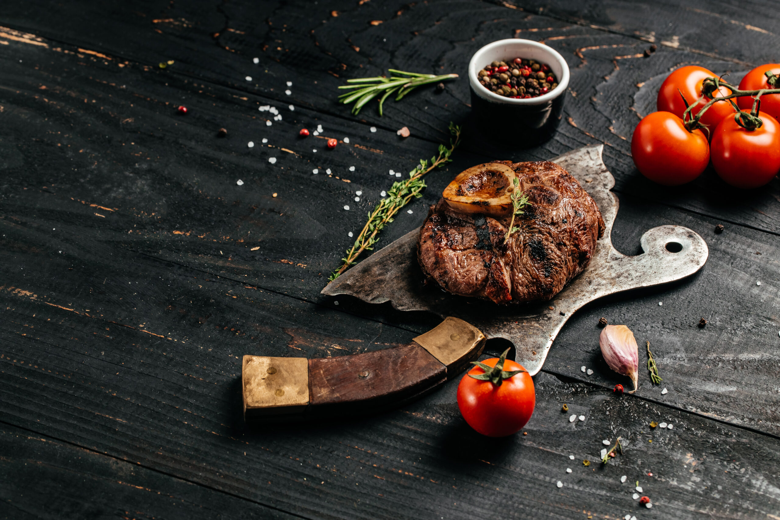 grilled veal Osso Buco steak on metal meat cleaver on black background. Top view.