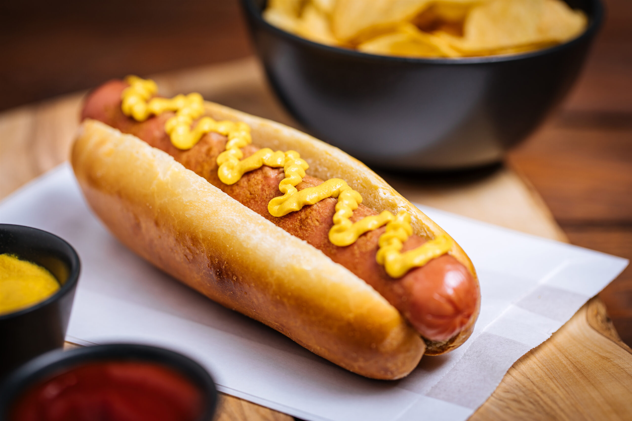 Hot Dog sausage and bun with ketchup and mustard sauce and lettuce and potato chips on Wooden Background