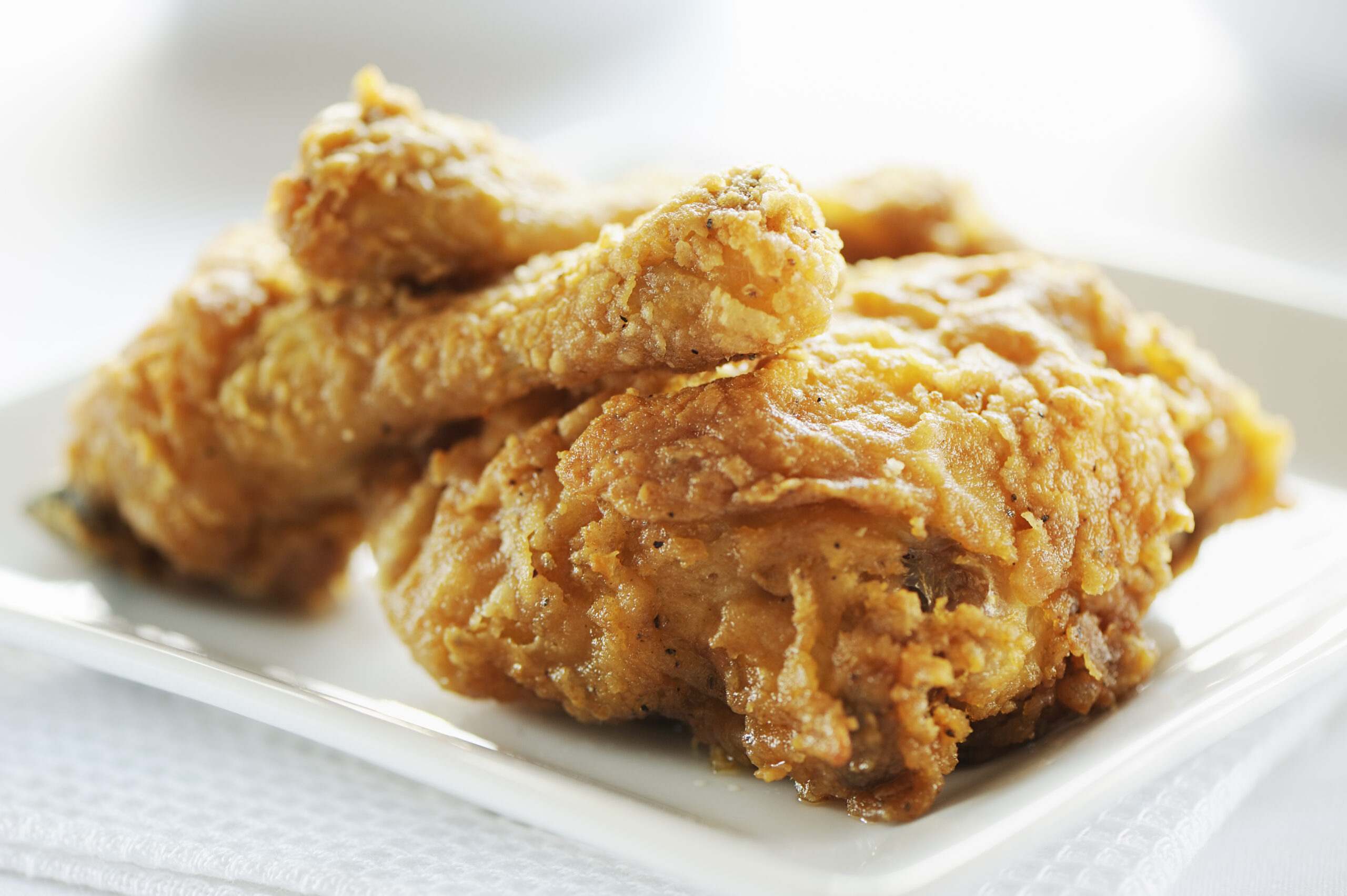Plate of crispy fried chicken on a white background. More fried chicken below...