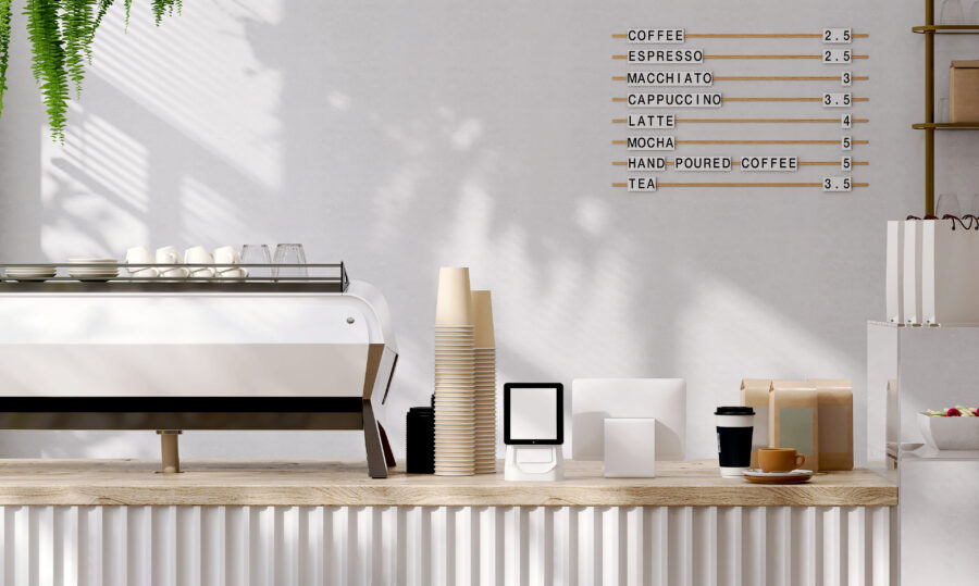 Modern and luxury design of cafe counter with wooden top, espresso machine, digital tablet computer cash register, stack of paper coffee cups with sunlight and leaf shadow from window on white wall