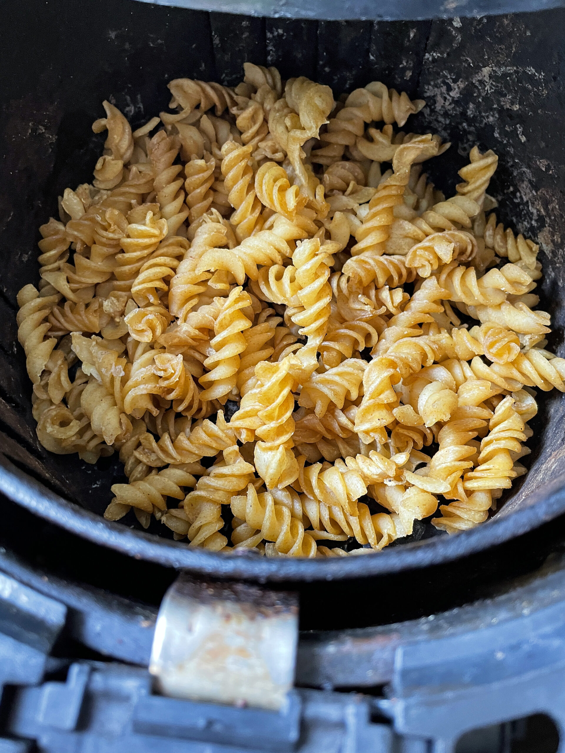 Stock photo showing close-up, elevated view of the inside of an air fryer with a pile of golden brown, freshly cooked, homemade pasta chips. Healthy cooking concept.