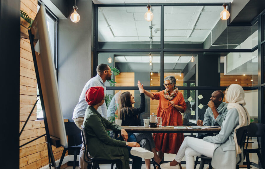 Successful businesswomen high fiving each other during an office meeting. Two cheerful businesswomen celebrating their achievement. Happy businesspeople working as a team in a multicultural workplace.