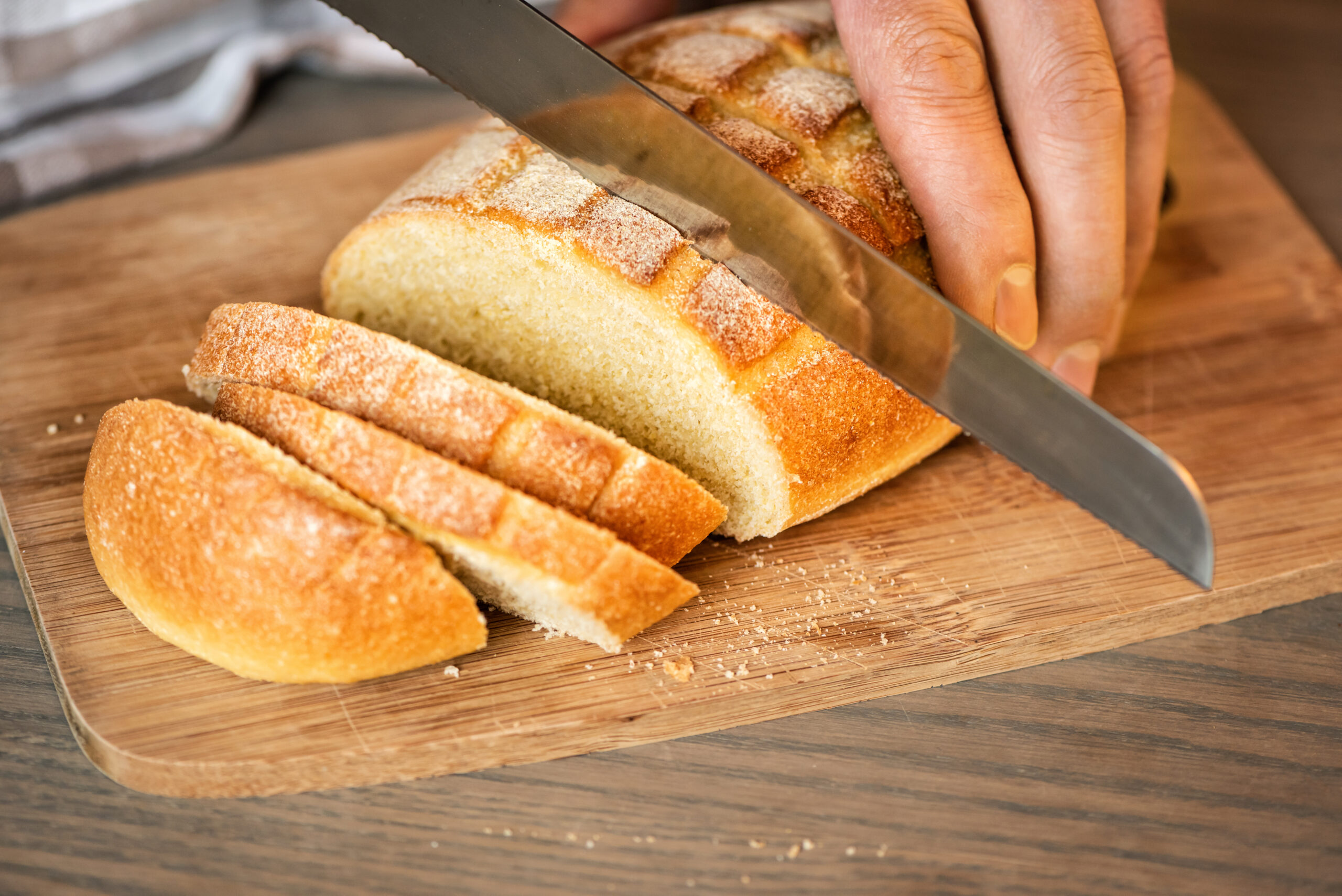 A man cuts bread with a serrated knife.