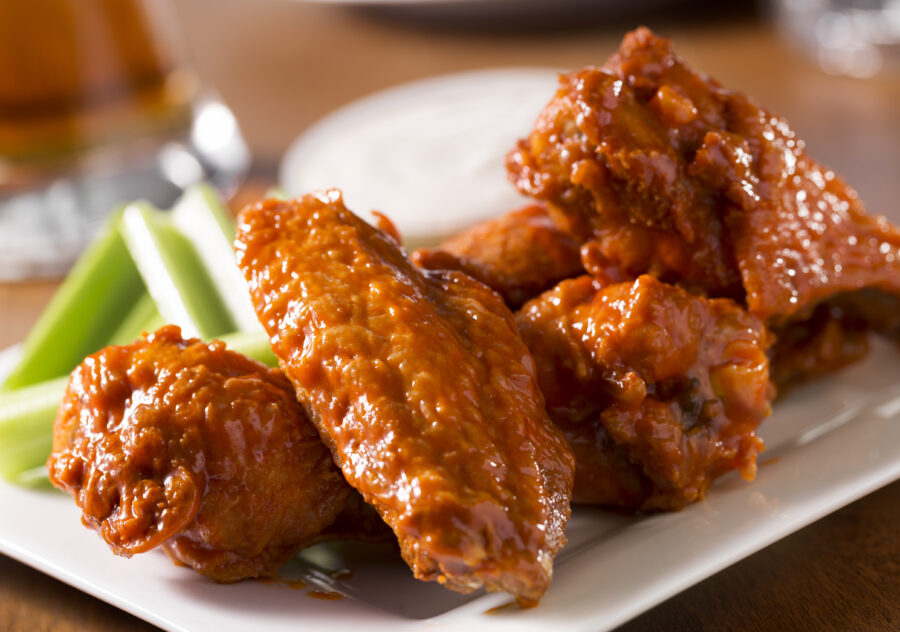 A plate of buffalo style chicken wings with celery and blue cheese with a beer on a bar or restaurant table.  