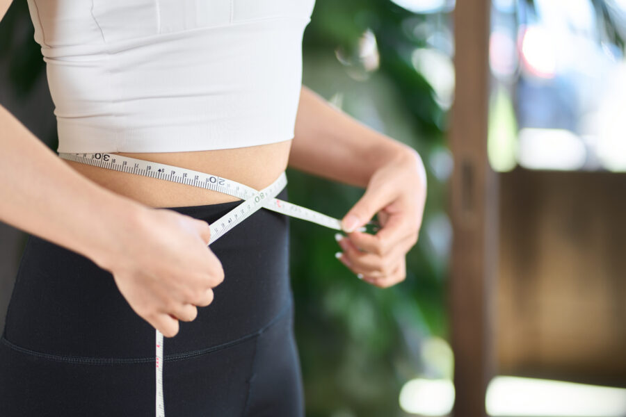 woman measuring her waist size with a tape measure