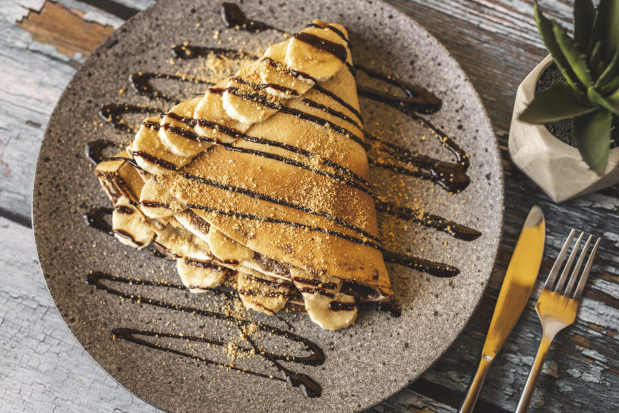 Chocolate pancake with bananas isolated on wooden background