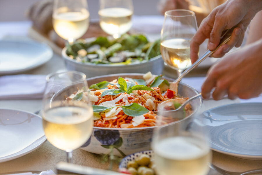 Close up of Serving spaghetti Bolognese on a table at sunset. There are glasses of wine and salad on the table