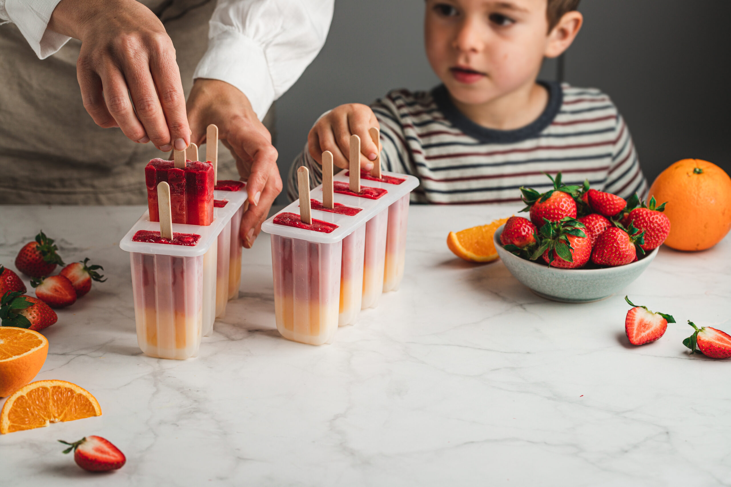 Close-up of woman and son taking out ice pop from moulds in the kitchen.