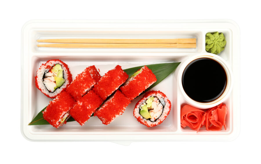 Close up take away set of Boston or California sushi rolls with red tobiko caviar and crab meat in disposable plastic tray isolated on white background, elevated top view, directly above