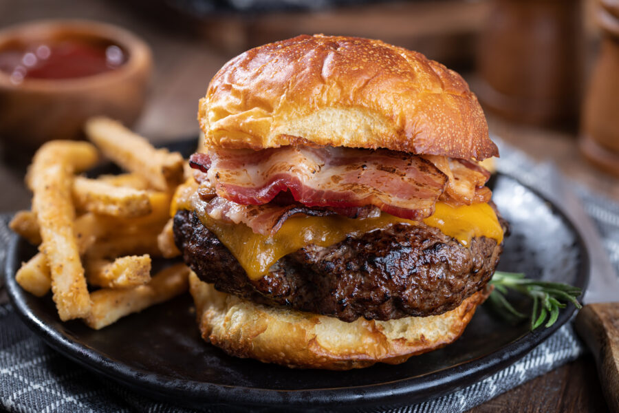 Closeup of a bacon cheeseburger on a toasted bun and french fries on a black plate