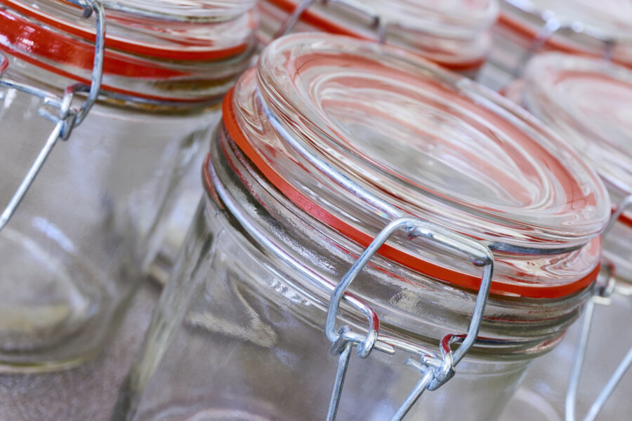 Closeup of empty glass canning jars or preserving containers with orange sealing ring in a row.