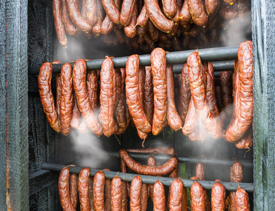 Closeup of hot smoky sausages from pork and beef meat hanging inside homemade smokery. Making tasty savoury charcuterie in smokehouse