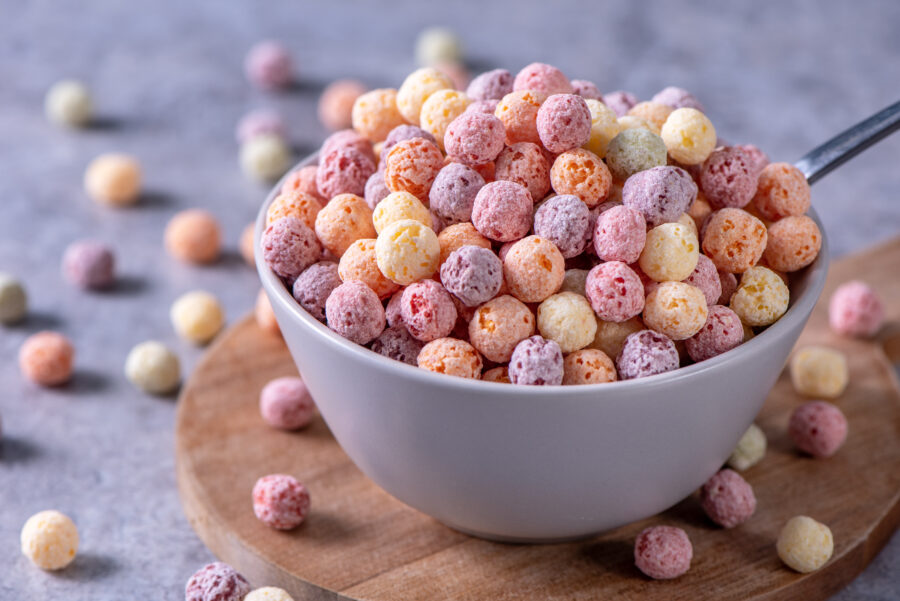 Colorful cereal corn balls mix, fruit flavor bowl sweets on gray cement background, close up