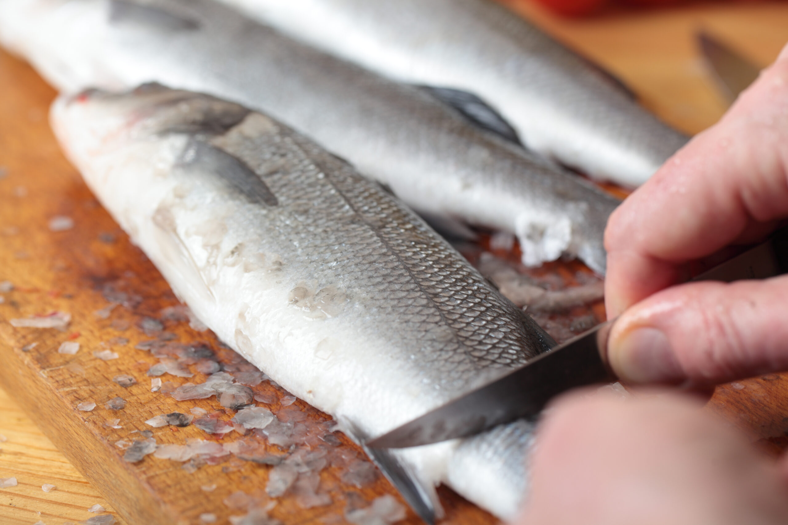 Cook cleaning a sea bass on a wooden cutting board