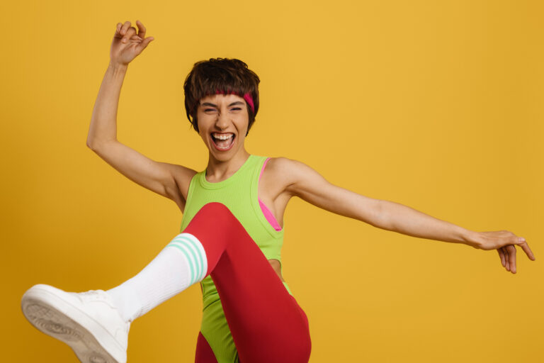 Excited fit woman in retro styled sports clothing dancing against yellow background