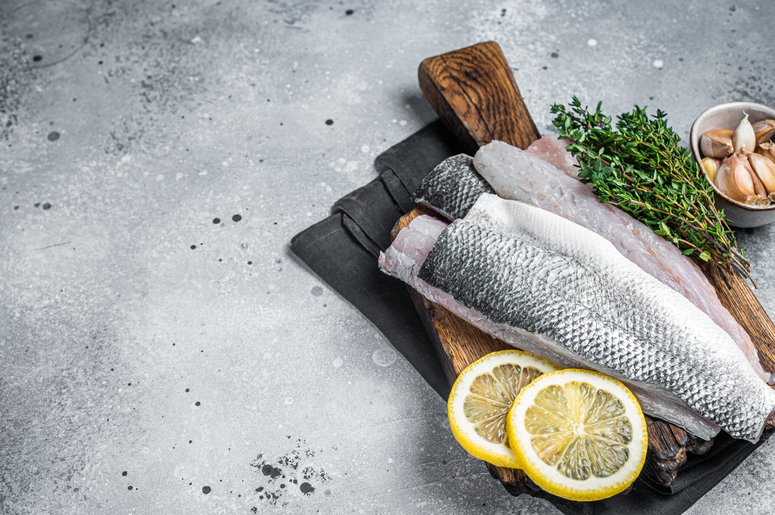 Fresh Raw Sea Bass fillets, Branzino fish with thyme and lemon. Gray background. Top view. Copy space.