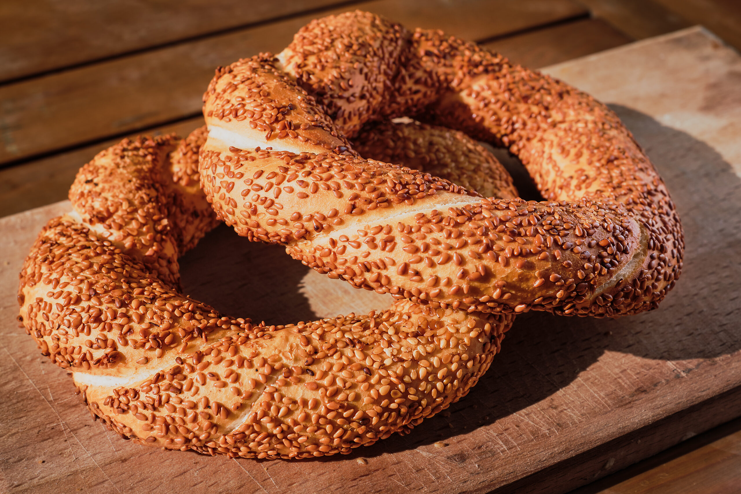 Freshly baked bagel with sesame seeds on a wooden table in the rays of sunlight. Turkish bagel simit close-up, fresh pastries for breakfast.