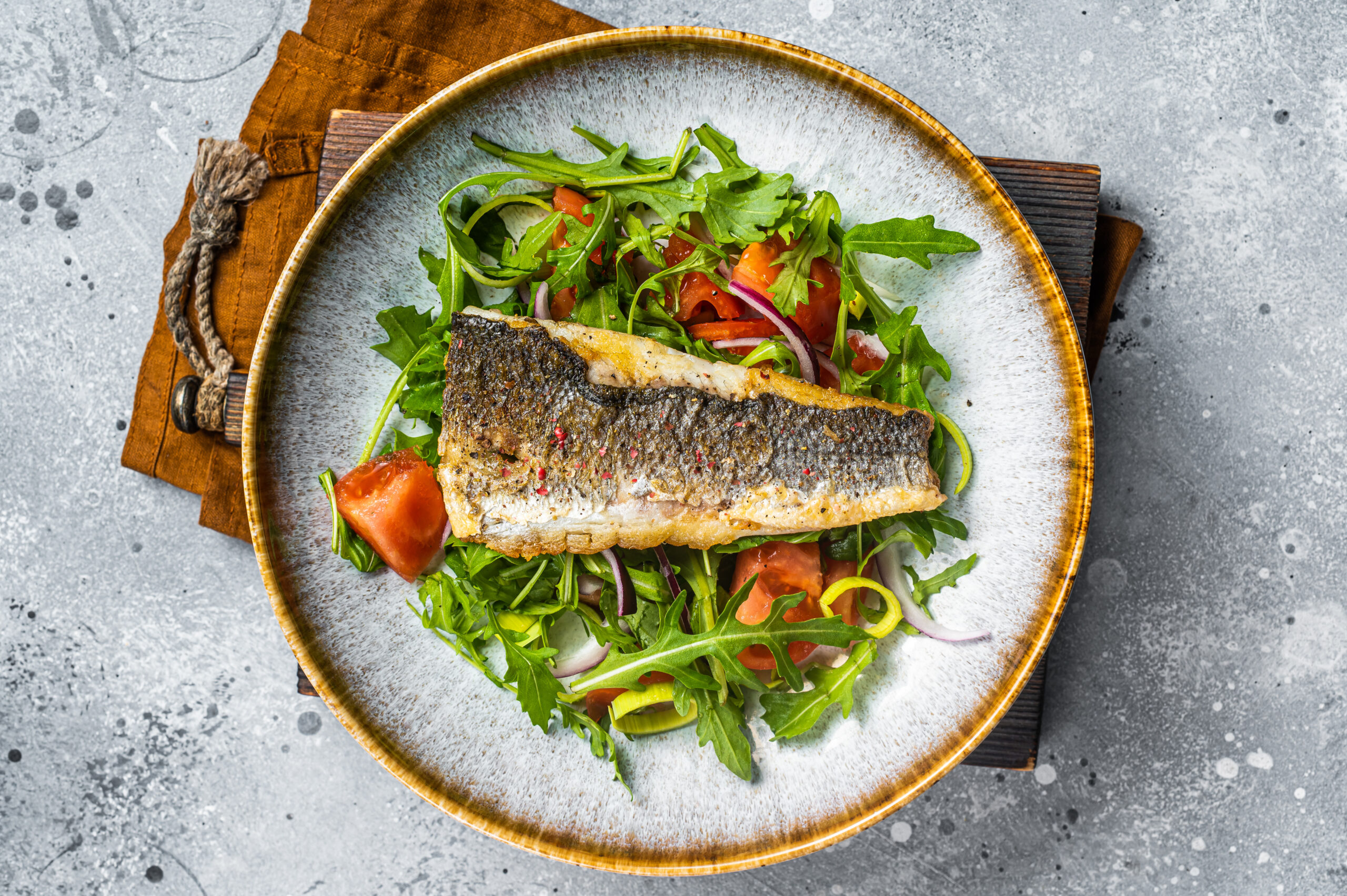 Fried sea bass branzino fillet with vegetable salad, Dicentrarchus fish. Gray background. Top view.