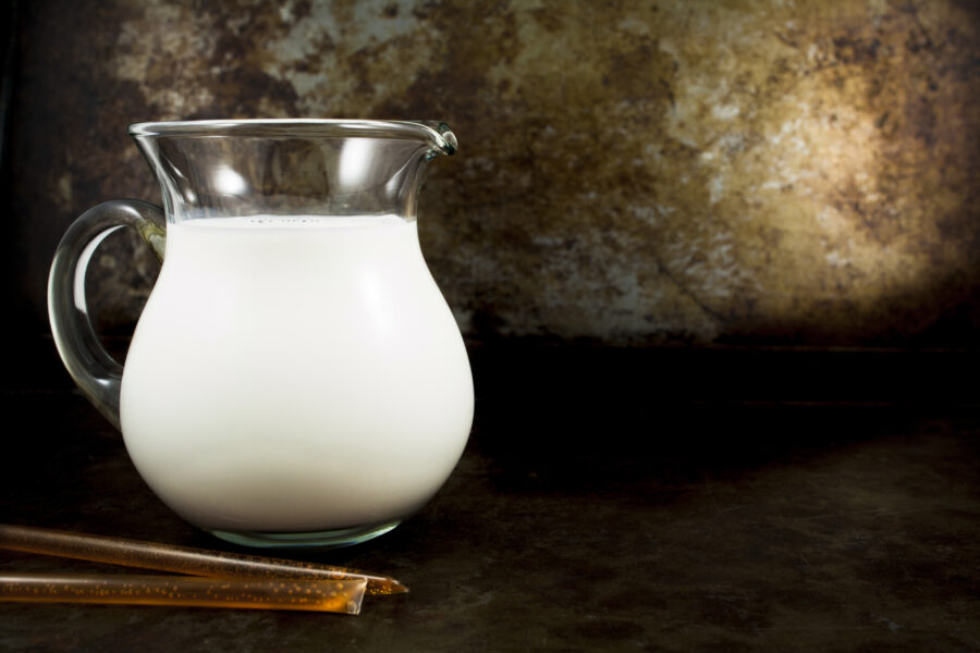 Glass pitcher of milk and honey sticks against a rustic backdrop