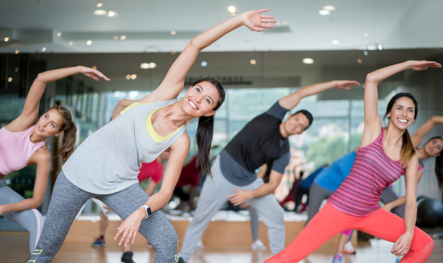 Group of people in an aerobics class at the gym stretching looking very happy