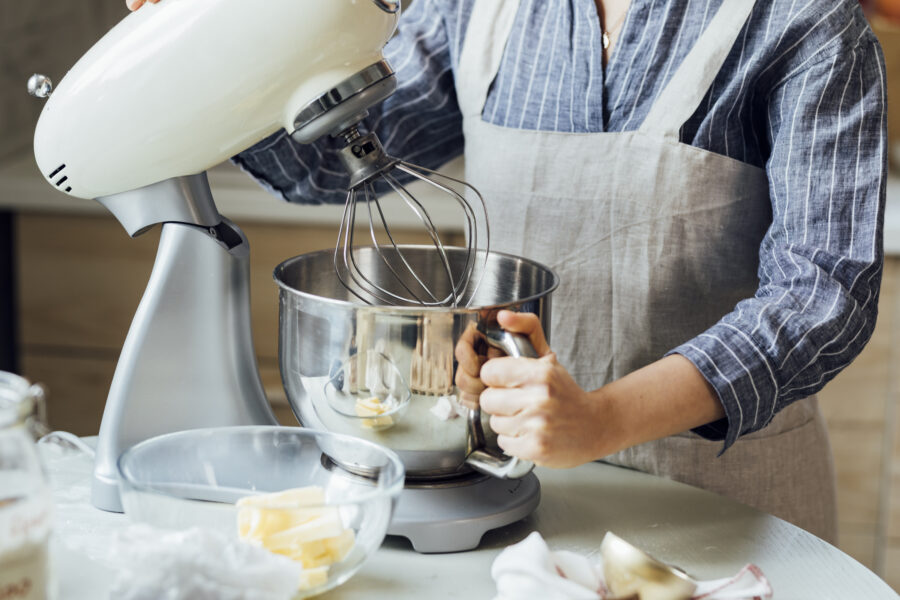 Hands of a woman in an apron using a stand mixer at home.