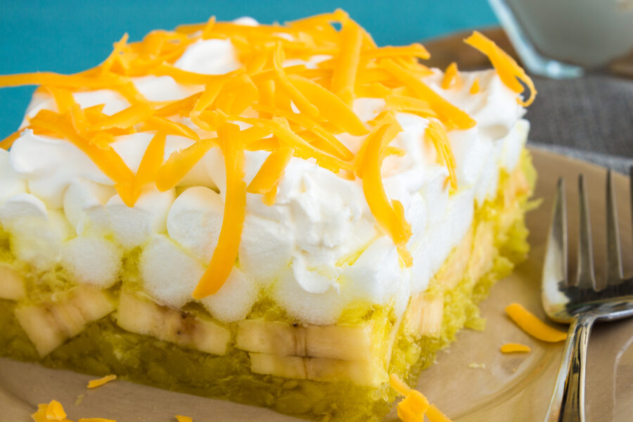 Hawaiian salad made with lemon jello, pineapple, banana, mini marshmallows, topped with whipped cream and cheddar cheese