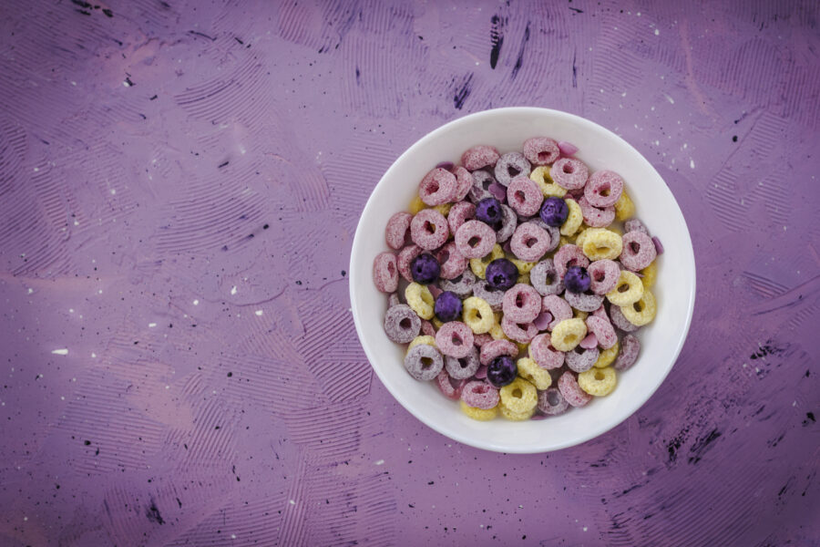 Healthy cereal loops with blueberry in a bowl. Multicolored loops on decorative violet background. 