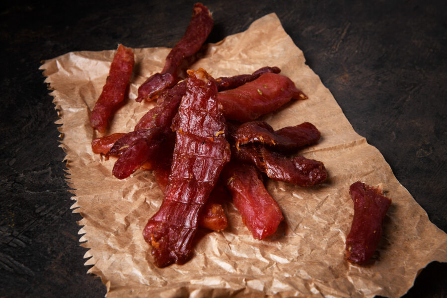 Jerky meat strips with spices and herbs on a paper on a dark background.