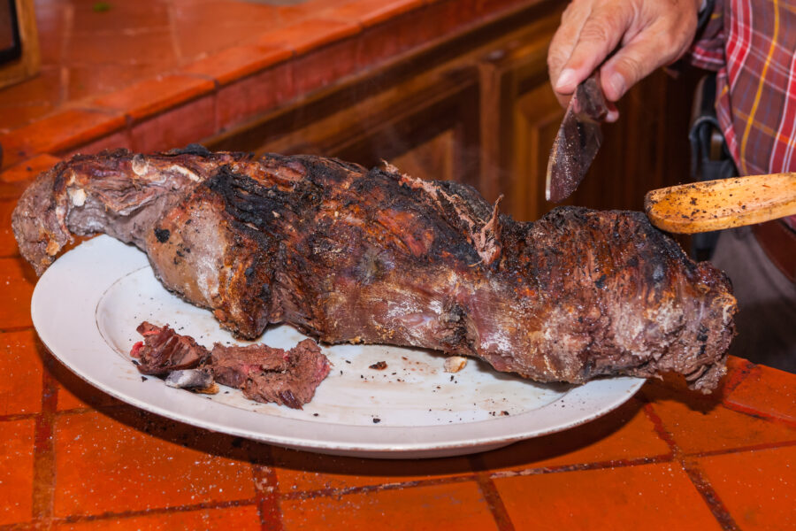 This portion lomo al trapo is now ready to be sliced up and served. The specks of white on the meat and the counter are actually salt crystals. The bits of black on the plate, are from the cloth that covered the meat while it was in the fireplace. Photo shot in the light of the fireplace; horizontal format.