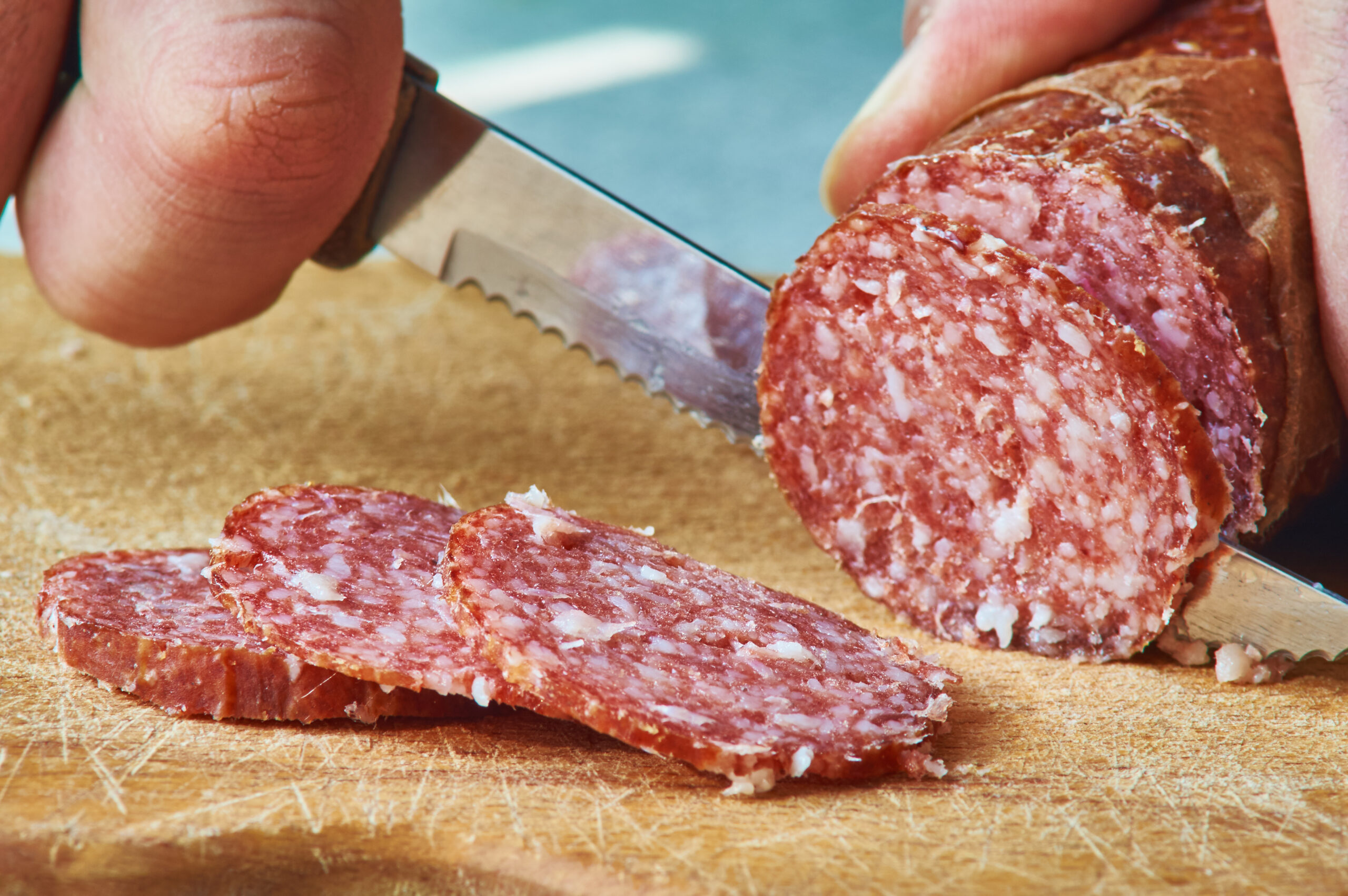 Male hand is cutting a sausage using serrated knife closeup