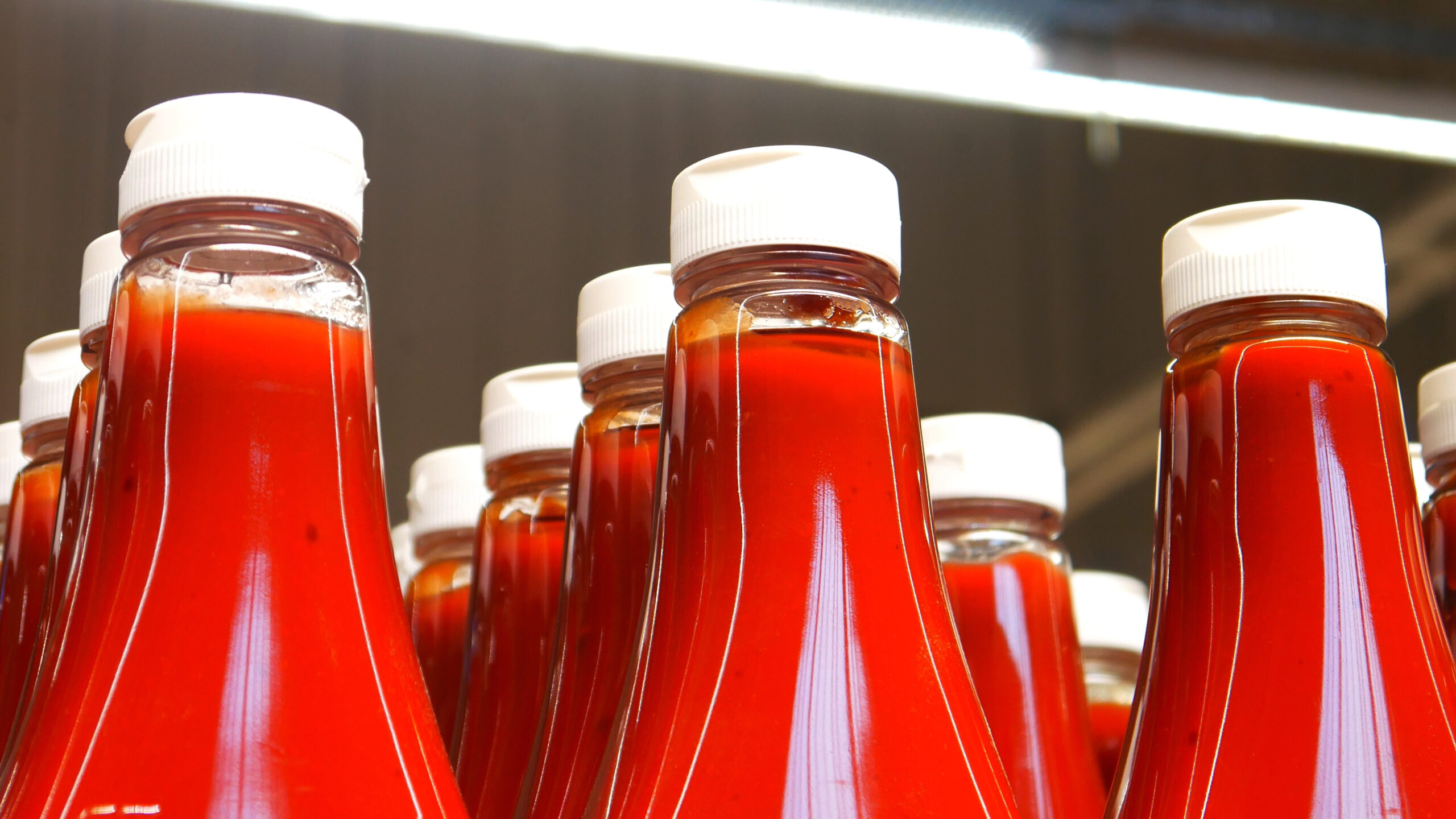 Many beautiful bottles of ketchup on a supermarket shelf close-up